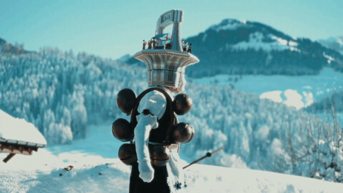 A gif from a short film about Silvesterchlausen in Switzerland, featuring a man in a costume with huge bells and a headdress dancing with snowy mountains in the background