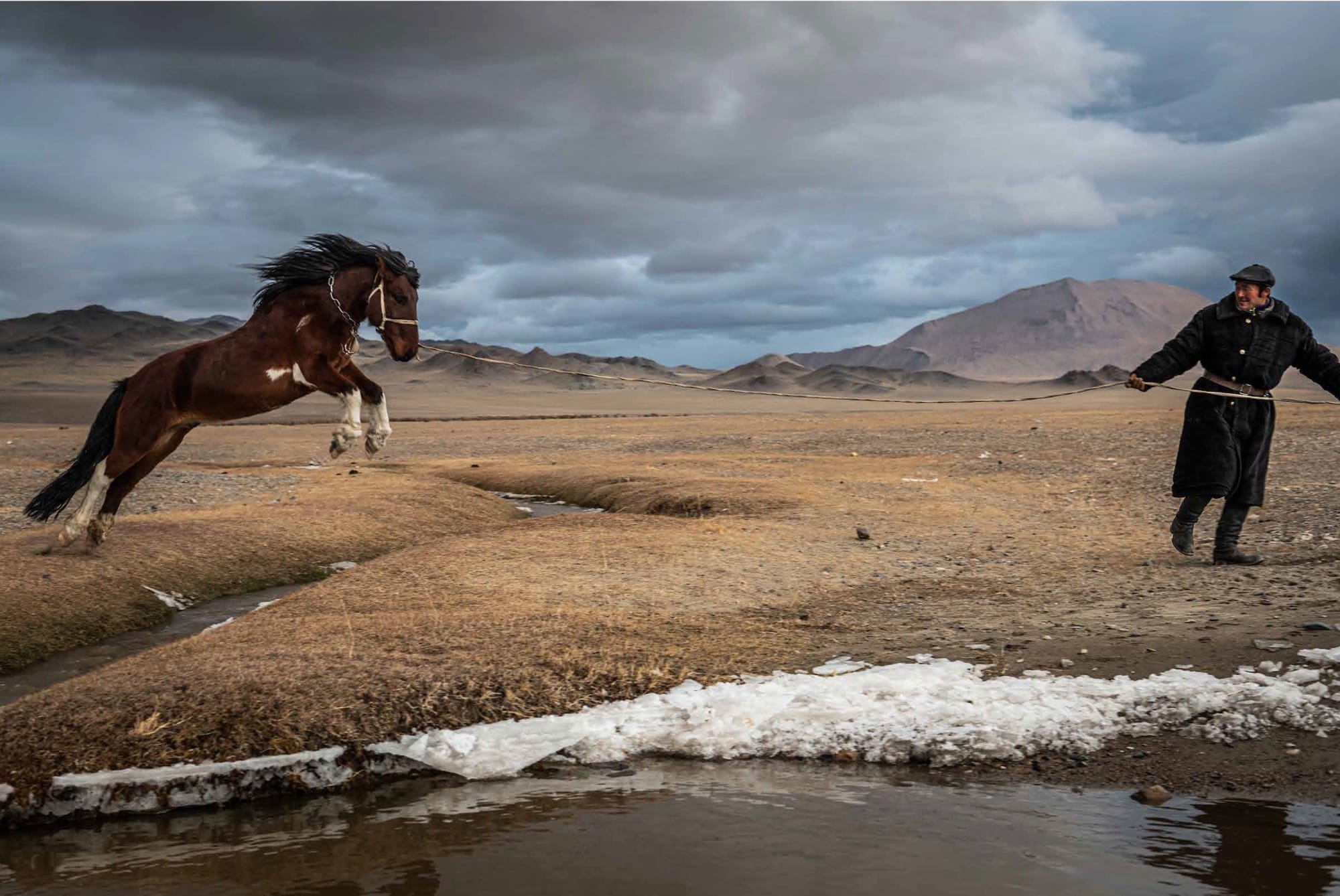 A photograph by Claire Thomas of a Kazakh man encouraging a large horse to leap over a stream