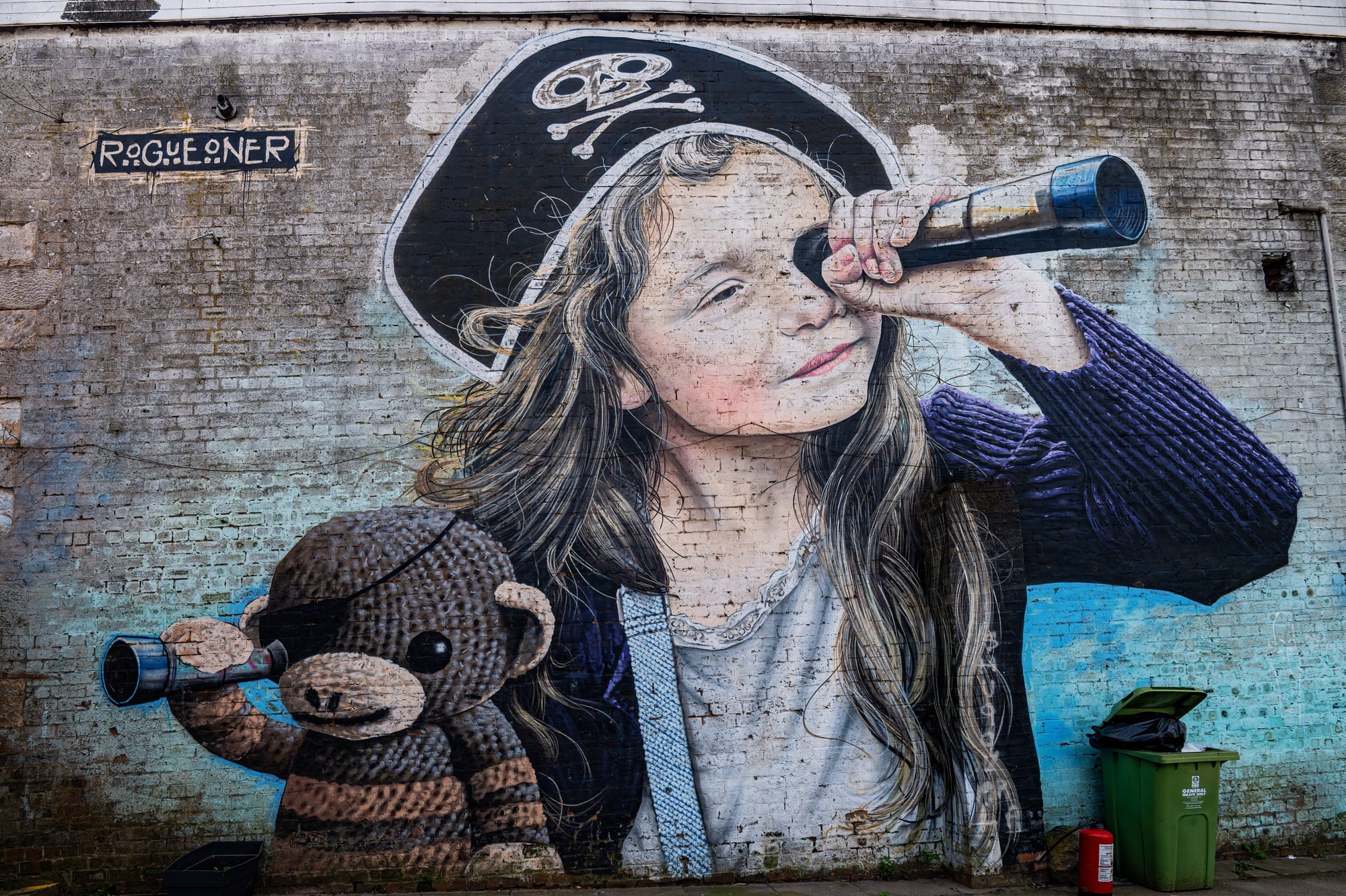 A mural by Rogue-one of a young girl with a pirate hat, looking through a spyglass, with her stuffed monkey toy also looking through a spyglass