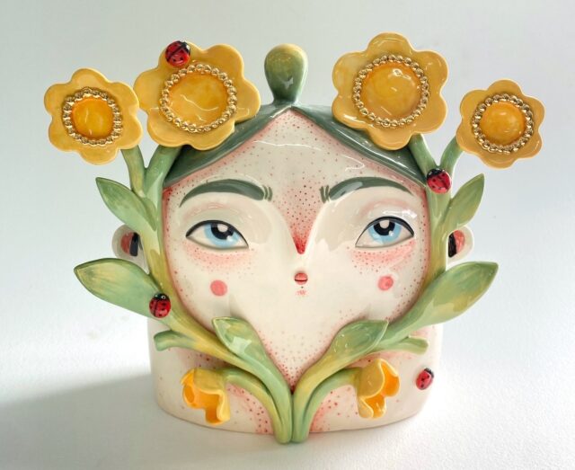 a ceramic sculpture by Abi Castillo of a head with green hair surrounded by yellow flowers