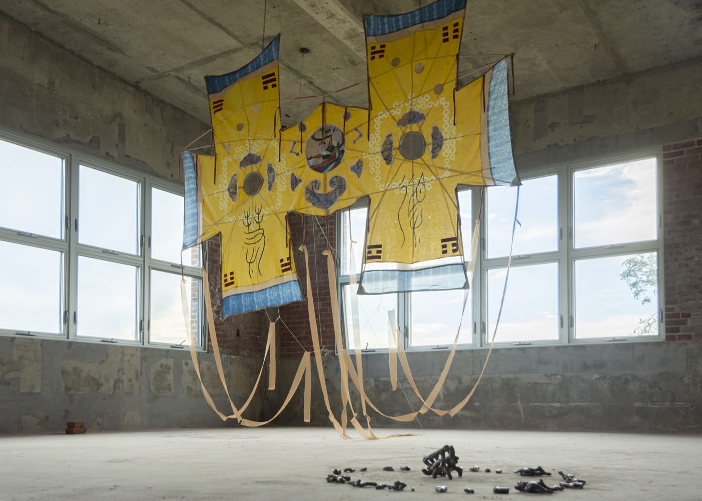 A large, yellow textile artwork by Hai-Wen Lin hangs in the middle of an industrial exhibition space.