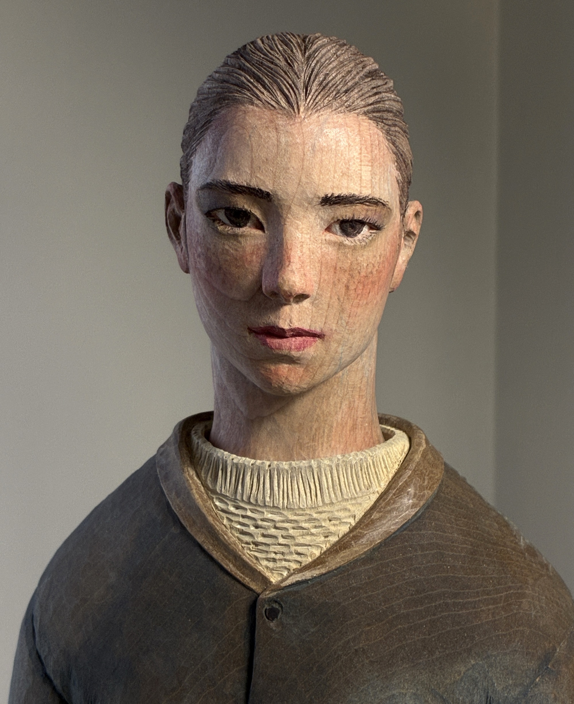 A detail of a figurative, painted wood sculpture of a young man by Shinsuke Inoue