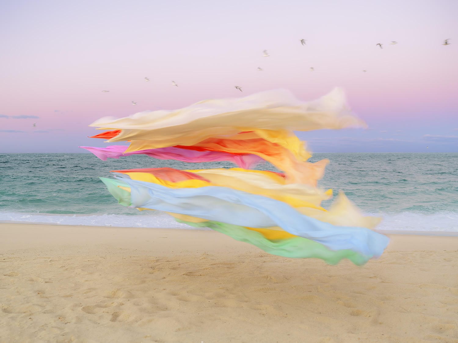 A photograph by Thomas Jackson of numerous pieces of colorful fabric that are seemingly suspended in the air on a beach