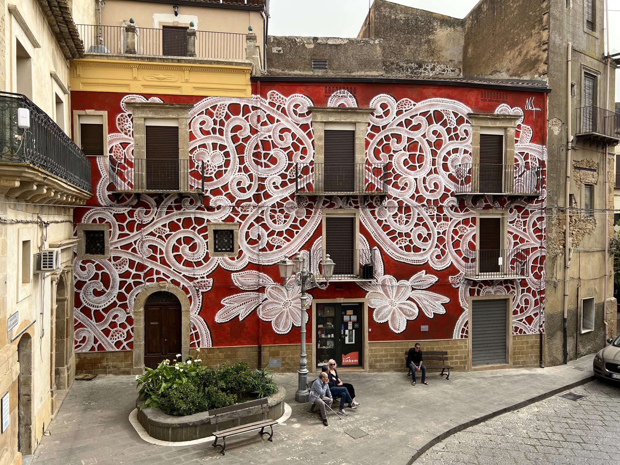 A wall mural on a building in the design of white lace with a red background by NeSpoon