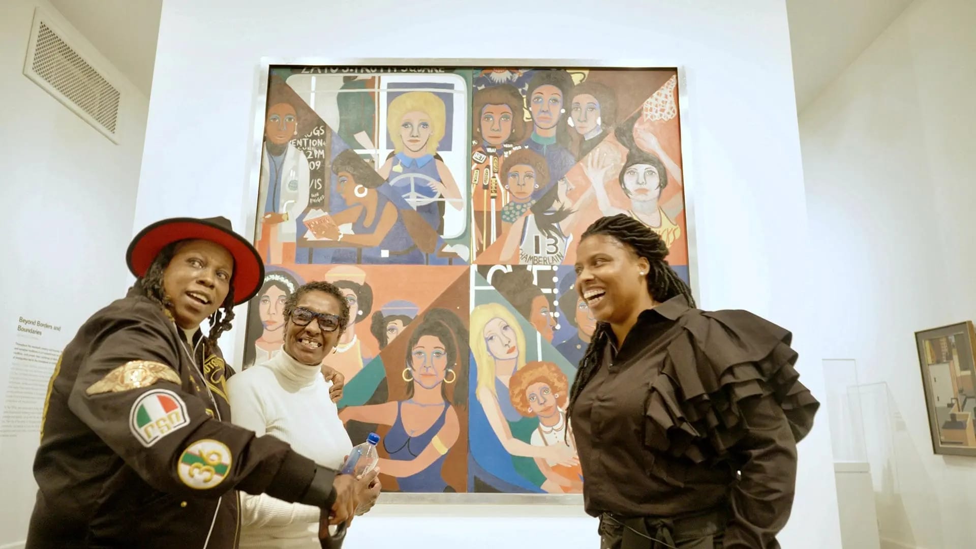 three artists stand in front of a vibrant mural of women in various professions