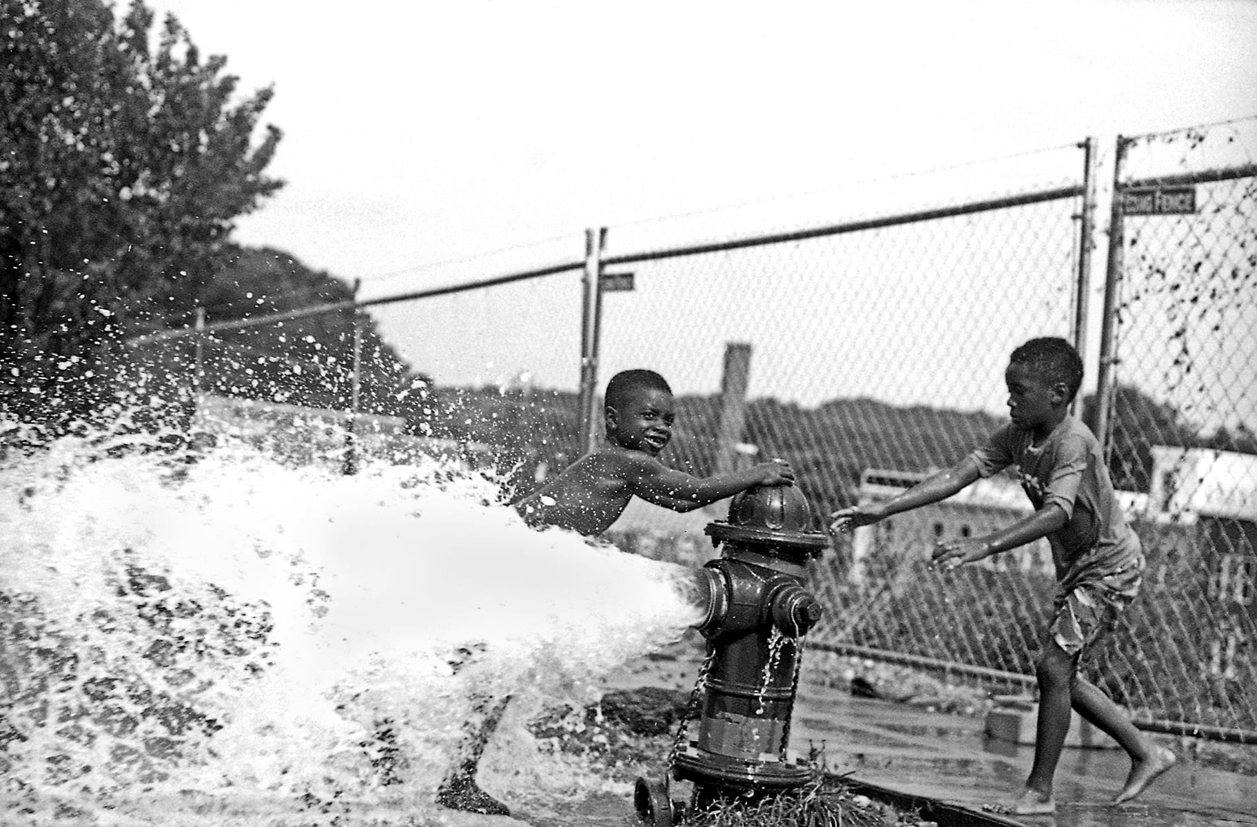 a black and white photo of children playing in a fire hydrant by beverly price