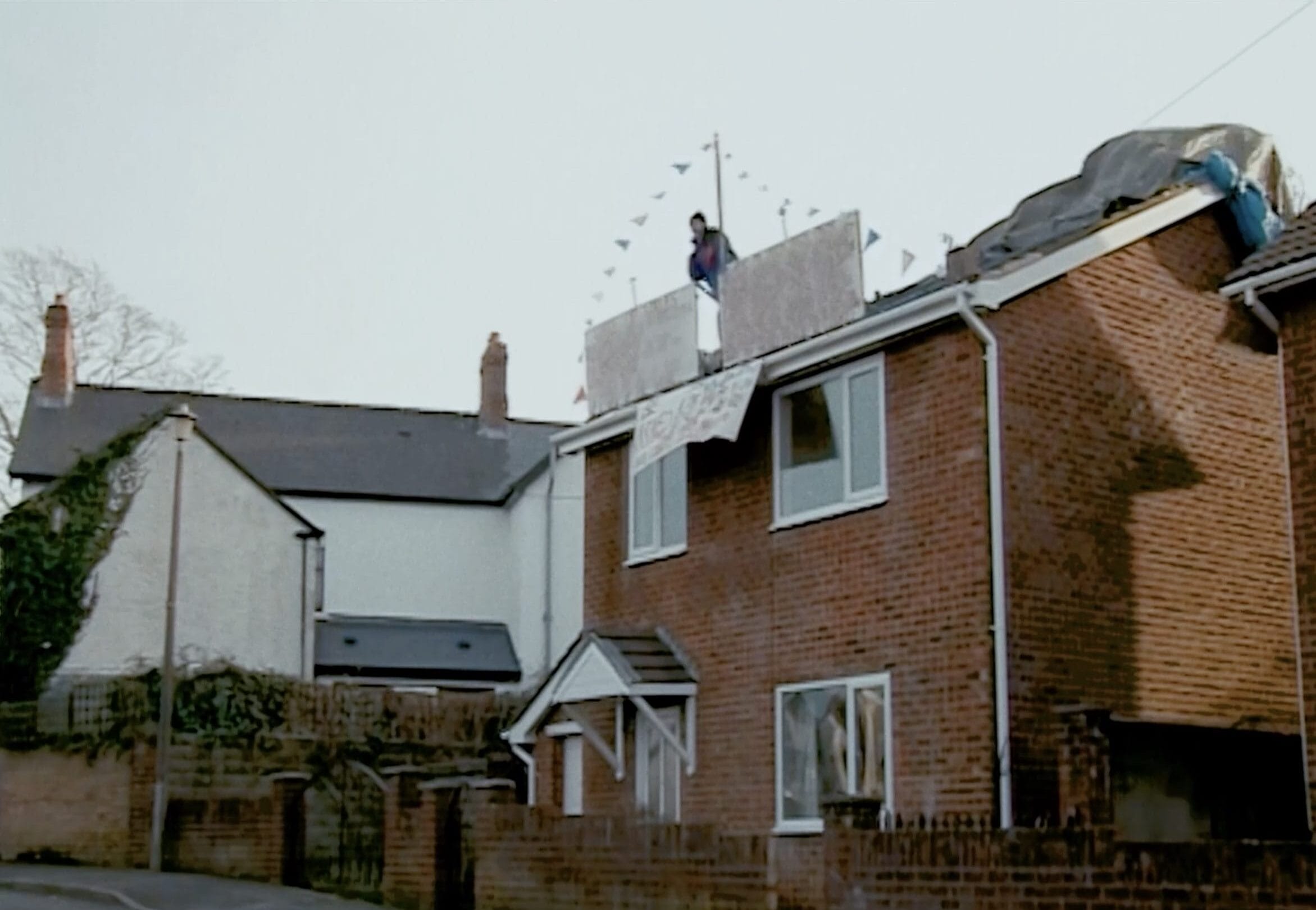 A still from archival footage of a man on top of house's roof