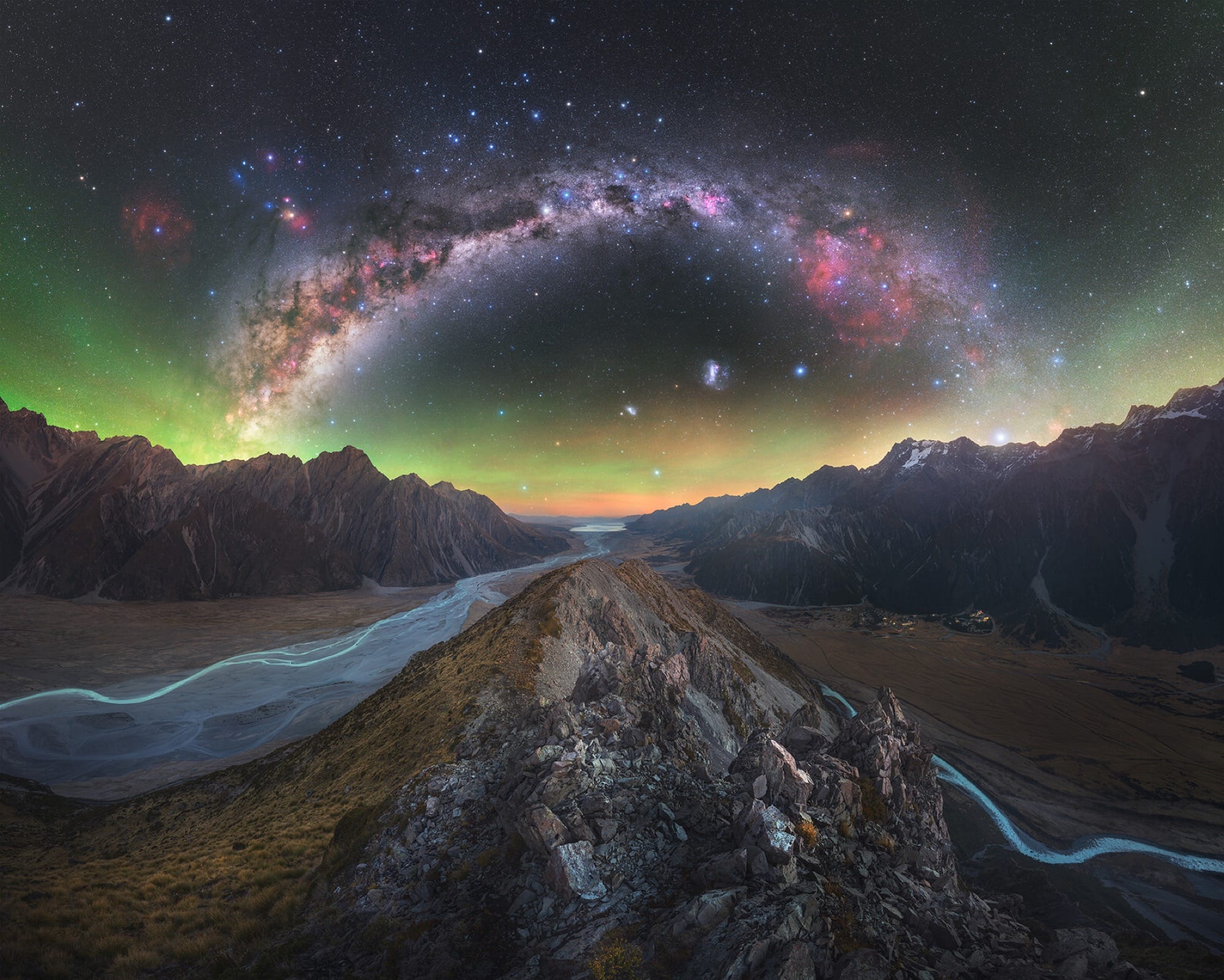 a dramatic wide-angle photo of a rocky landscape with aurora borealis and the Milky Way above